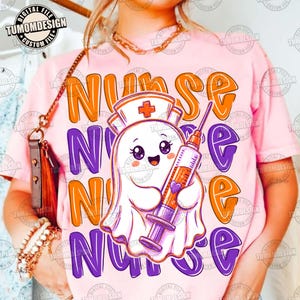 May include: A light pink t-shirt featuring a cartoon ghost wearing a nurse cap and holding a syringe. The word NURSE is printed in large, wavy orange and purple letters behind the ghost. The design includes a small purple heart on the syringe.