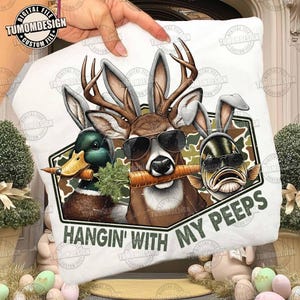 May include: White pillow with a humorous design featuring a duck, deer, and fish wearing sunglasses and bunny ears, each holding a carrot. The text "HANGIN' WITH MY PEEPS" is printed below the characters. The design is set against a camouflage background.
