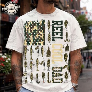 May include: A white short-sleeve t-shirt featuring a graphic design of a flag made from camouflage patterns and fishing lures. The text REEL COOL DAD is printed in a bold, block font with a camouflage fill next to the fishing lure illustrations.