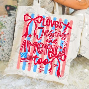 May include: A cream-colored tote bag with a patriotic design. The bag features red and blue vertical stripes, red bows, stars, and the text "Loves Jesus and America too" in red. An American flag is also displayed.
