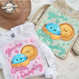 Puede incluir: Dos sudaderas con el texto "You're a Glitter Dumpling". Una es blanca con detalles rosas, la otra es beige con detalles turquesa. Cada una presenta una caricatura de una bola de masa hervida en una vaporera de bambú. El diseño incluye estrellas y un estampado de leopardo.