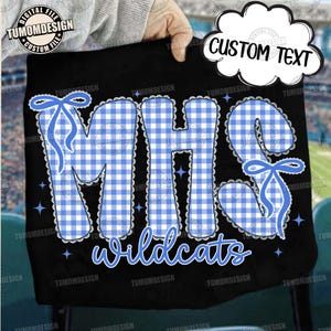 Peut inclure: Un article en tissu noir présentant les lettres MHS dans un motif vichy bleu et blanc avec une bordure en dentelle blanche et des nœuds bleus. Le mot wildcats est imprimé en dessous en écriture bleue. De petites étoiles bleues sont éparpillées.