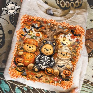 May include: A light-colored t-shirt featuring a graphic of three bear characters in Halloween costumes: one as a pumpkin, one as a skeleton, and one as a mummy. The design includes autumn trees, lanterns, bats, and a leopard print border.