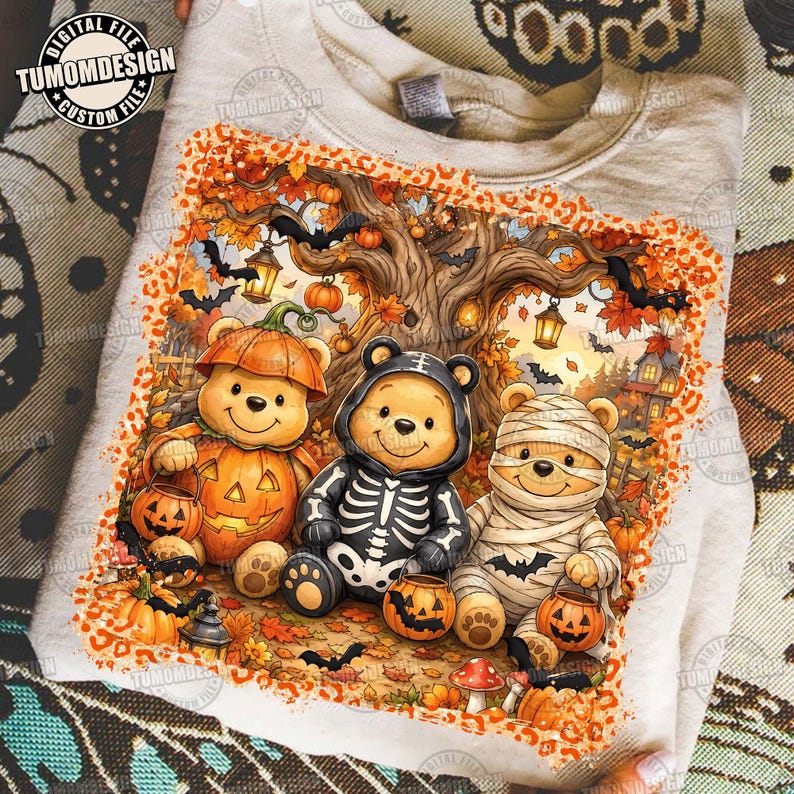 May include: A light-colored t-shirt featuring a graphic of three bear characters in Halloween costumes: one as a pumpkin, one as a skeleton, and one as a mummy. The design includes autumn trees, lanterns, bats, and a leopard print border.