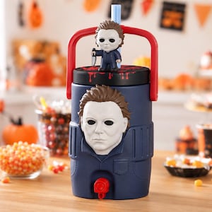 May include: A dark blue beverage cooler featuring a molded 3D Michael Myers mask on the front, a red carrying handle, and a black lid with a small Michael Myers figure holding a knife. A light blue straw extends from the top of the lid.