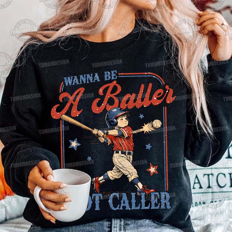 May include: Black sweatshirt with a baseball-themed graphic. The design features a baseball player swinging a bat, with the text "WANNA BE A Baller NOT CALLER" in red and blue. Stars and a baseball complete the design.