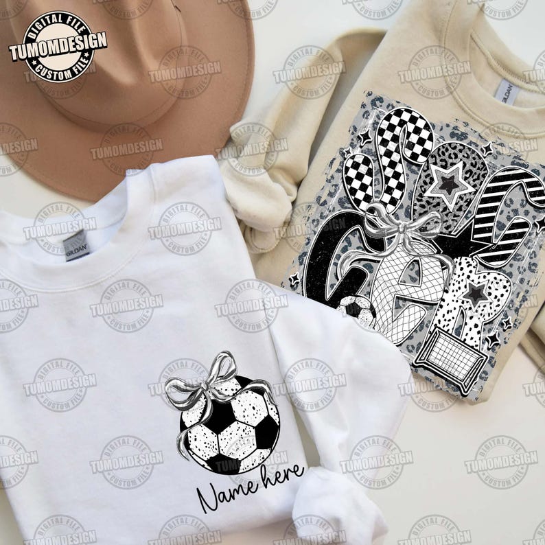 May include: White sweatshirt with a black and white graphic of a soccer ball with a bow on top. The text "Name here" is below the graphic.