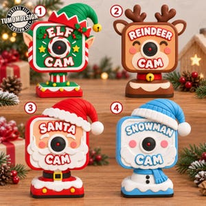 May include: Four decorative holiday camera figures labeled Elf Cam, Reindeer Cam, Santa Cam, and Snowman Cam. Each square-shaped camera features a central lens, festive character-themed hats, and colorful bases with holiday-inspired details.
