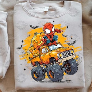 May include: A light beige sweatshirt featuring a Halloween-themed graphic. The design includes a cartoon Spider-Man character sitting on a monster truck filled with carved pumpkins. Bats, spiderwebs, and stars complete the festive scene.