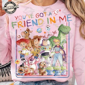 Può includere: Felpa rosa chiaro con una grafica colorata dei personaggi di Toy Story. Il testo "YOU'VE GOT A FRIEND IN ME" è visualizzato sopra i personaggi. Il design include un razzo, stelle e un pianeta.
