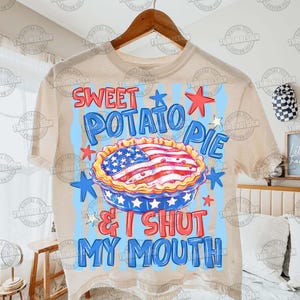 May include: Beige t-shirt with a graphic design featuring a sweet potato pie decorated with an American flag. The text reads "SWEET POTATO PIE & I SHUT MY MOUTH" in red and blue. The design includes stars.