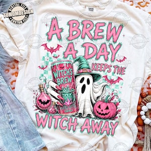 以下が含まれることがあります： 魔女の帽子をかぶった幽霊が「Witch's Brew」と書かれたピンクのエナジードリンク缶を持ち、ピンクのカボチャ、コウモリ、そしてピンクと黒の文字で「A BREW A DAY KEEPS THE WITCH AWAY」と描かれたクリーム色のTシャツ。