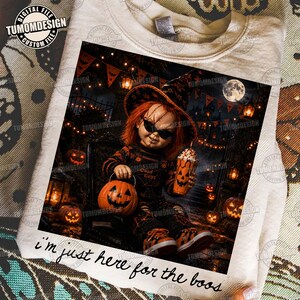 May include: A beige sweatshirt featuring a graphic of a doll with orange hair, wearing a hat and sunglasses, holding a pumpkin bucket and a pumpkin-themed drink. The text "I'm just here for the boos" is printed below the graphic in black script.