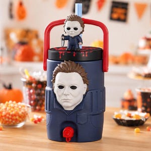 May include: A dark blue beverage dispenser featuring a molded Michael Myers mask on the front, a red handle, and a black lid with a small Michael Myers figure holding a knife. The lid has red blood splatter patterns and a light blue straw.