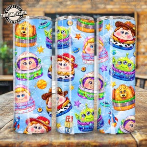 May include: A cylindrical tumbler featuring a repeating pattern of cartoon characters in space-themed vehicles against a light blue sky background. The design includes stars, planets, and small rockets, with characters wearing hats and helmets.
