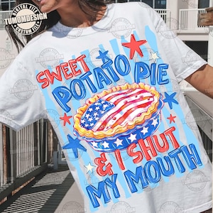 May include: White t-shirt with a graphic design featuring a sweet potato pie decorated with the American flag. The text reads "Sweet Potato Pie & I Shut My Mouth" in red and blue.