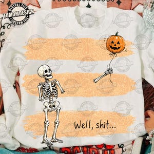 May include: A white long-sleeve sweatshirt featuring a graphic of a skeleton looking at a detached skeletal arm holding a pumpkin balloon. The design includes orange brushstroke stripes with a spiderweb pattern and the text Well, shit...
