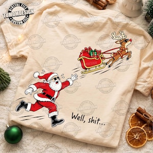 May include: A cream-colored t-shirt featuring a graphic of Santa Claus running after a flying red sleigh pulled by a reindeer. Both characters wear sunglasses. The text "Well, shit..." is printed in black below the running Santa figure.