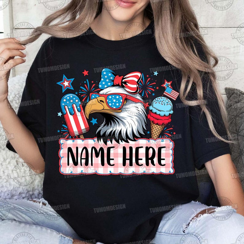 May include: Black t-shirt featuring a patriotic design with an eagle wearing sunglasses, a bow, and ice cream. The design includes the text "NAME HERE" in a red and white checkered frame, and stars.