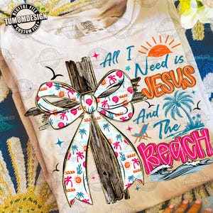 Könnte beinhalten: Cremefarbenes T-Shirt mit einem Holzkreuz, das mit einer gemusterten Schleife verziert ist. Die Schleife zeigt Palmen, Sonnen und Kakteen. Der Text auf dem Shirt lautet "All I Need is Jesus And The Beach" in verschiedenen Farben. Eine Sonne, eine Palme und Wellen sind ebenfalls abgebildet.