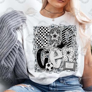 May include: White t-shirt with a black and white graphic design of the word "Soccer" with a soccer ball and a goal net. The graphic has a checkered, leopard print, and striped pattern.