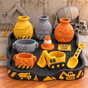 Puede incluir: Un set de construcción que incluye una bandeja negra con gráficos de excavadora y camión volquete, con tres recipientes redondos en amarillo, gris y naranja, un cuenco gris, un cono de tráfico naranja, una pala amarilla y un letrero de Work Zone.
