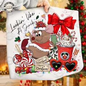 Puede incluir: Un gráfico blanco con temática navideña que presenta un ratón de dibujos animados con un gorro de Papá Noel, sosteniendo un trozo de queso. El diseño incluye un lazo rojo, bastones de caramelo, gafas de sol en forma de corazón y el texto "Lookin' like A Snack" y "Merry Christmas".