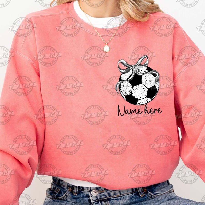 May include: A pink sweatshirt with a black and white soccer ball with a bow on top. The text "Name here" is printed below the soccer ball.