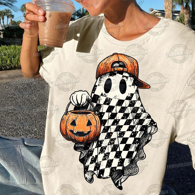 K&ouml;nnte beinhalten: Ein cremefarbenes T-Shirt mit einem Halloween-Motiv. Das Design zeigt einen Geist mit einer orangefarbenen Baseballkappe, der einen orangefarbenen K&uuml;rbis-Laterne h&auml;lt. Der K&ouml;rper des Geistes hat ein schwarz-wei&szlig;es Schachbrettmuster. Das T-Shirt hat den Text "TUMOMDESIGN".