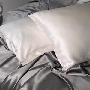 May include: Two white satin pillowcases on a gray satin bed sheet. The pillowcases are smooth and wrinkle-free.