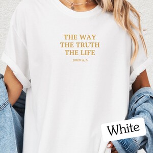 Op de afbeelding: Wit T-shirt met de tekst "THE WAY THE TRUTH THE LIFE" en "JOHN 14:6" in gouden letters.