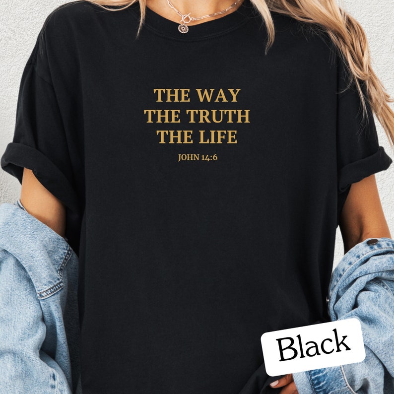Op de afbeelding: Zwart T-shirt met de tekst "THE WAY THE TRUTH THE LIFE JOHN 14:6" in gouden letters.