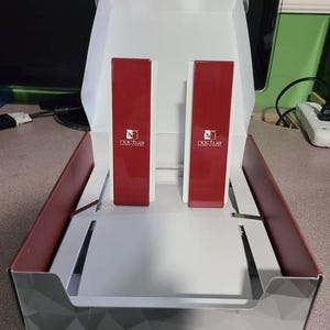 May include: A white box with a red and gray geometric pattern on the bottom. The box is open and contains two red boxes with the word "Noctua" printed on them.