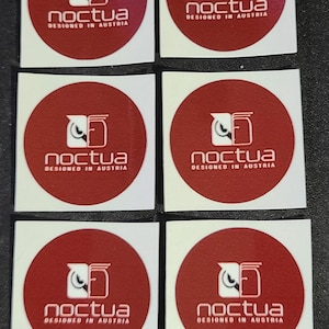 May include: Ten round stickers with a red background and white logo. The logo is a stylized owl with the word "noctua" and the text "designed in Austria" below it.
