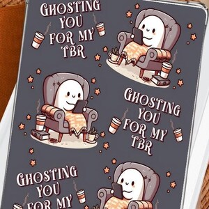 Könnte beinhalten: Ein druckbares Kindle-Einsatzdesign mit einem Geist, der in einem Sessel mit einer Tasse Kaffee ein Buch liest. Der Text lautet "Ghosting you for my TBR".
