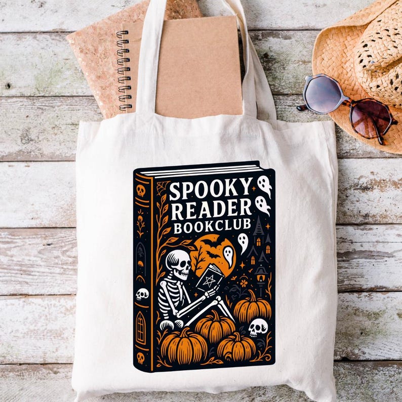 Pode incluir: Saco de tote branco com um design tem&aacute;tico de Halloween. O design inclui um esqueleto lendo um livro, ab&oacute;boras, fantasmas e o texto "Spooky Reader Bookclub". Um chap&eacute;u de palha e &oacute;culos de sol s&atilde;o vis&iacute;veis.