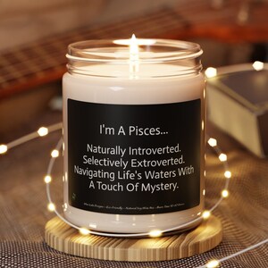 May include: A white candle in a glass jar with a black label that reads "I'm A Pisces... Naturally Introverted. Selectively Extroverted. Navigating Life's Waters With A Touch Of Mystery."