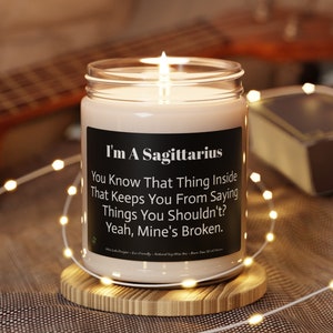 May include: A white candle with a black label that reads "I'm A Sagittarius You Know That Thing Inside That Keeps You From Saying Things You Shouldn't? Yeah, Mine's Broken."