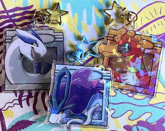 May include: Three holographic keychains featuring different Pokemon characters. The first keychain features a white and blue Pokemon with a blue background. The second keychain features a red and orange Pokemon with a yellow background. The third keychain features a purple and blue Pokemon with a blue background.