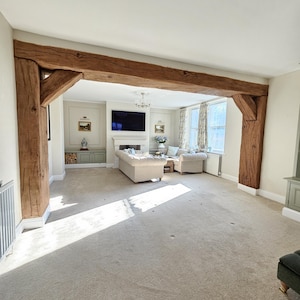 May include: A spacious living room with a neutral color palette. The focal point is a large, exposed wooden beam that frames the entrance. The room features a beige carpet, a white ceiling, and a fireplace with a mounted television.