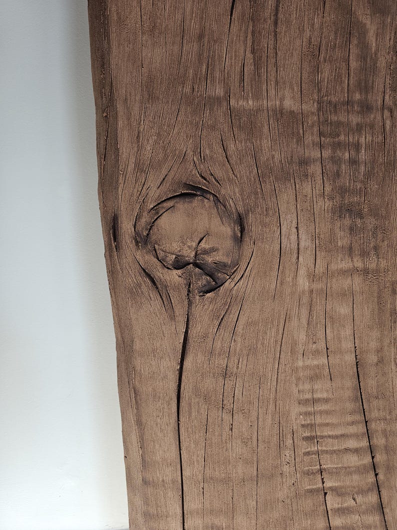 May include: Close-up of a weathered, brown wooden plank with a prominent knot. The wood grain is visible, with dark lines and textures. The plank has a natural, rustic appearance, with a rough, uneven edge.