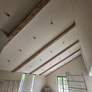 May include: Interior view of a room with a high, angled ceiling. The ceiling features exposed wooden beams and recessed lighting. The walls are painted a neutral color, and the room appears to be under construction, with a metal scaffolding visible.