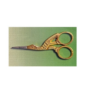 May include: Gold-colored, decorative scissors with a bird design. The scissors are closed and the blades are sharp. The brand name "Beadsmith" is printed on the blade.