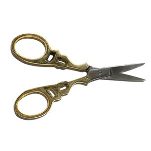 May include: Gold-toned decorative scissors with a silver blade. The scissors have a detailed design on the handles.