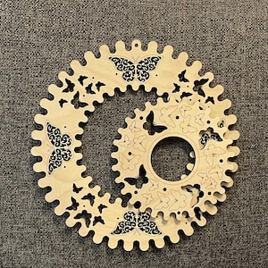 May include: A wooden wall decor with a circular design featuring multiple layers of intricate butterfly cutouts. The butterflies are arranged in a spiral pattern and have a black and white design.