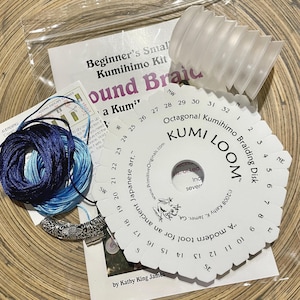 May include: A beginner's Kumihimo braiding kit with a white plastic octagonal loom, a white plastic braiding disk, blue and light blue silk cords, and a silver metal toggle clasp. The kit includes instructions for making a round braid.