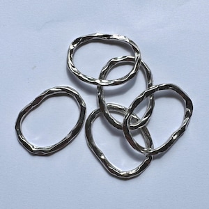May include: A collection of silver-colored, irregularly shaped rings, some linked together. The rings have a textured surface and appear to be made of metal. The rings are displayed against a white background.