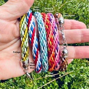 May include: A set of seven braided cords with different color combinations. The cords are labeled with names like "Calm Ocean", "Pinks & Purples", "Cappuccino", "Foliage", "Red White Blue", "Red Flames".