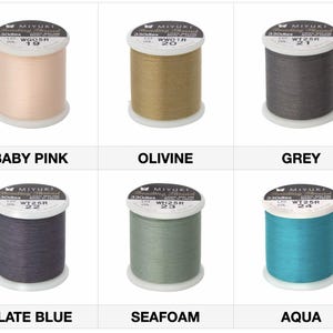 May include: Six spools of Miyuki beading thread in various colors: baby pink, olivine, grey, slate blue, seafoam, and aqua. Each spool is labeled with the color name and product information. The thread is made of nylon and is 330 dtex.