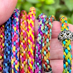 May include: Assortment of colorful braided cords with a silver heart charm. The cords are made of multiple strands of colorful thread woven together in a braided pattern.